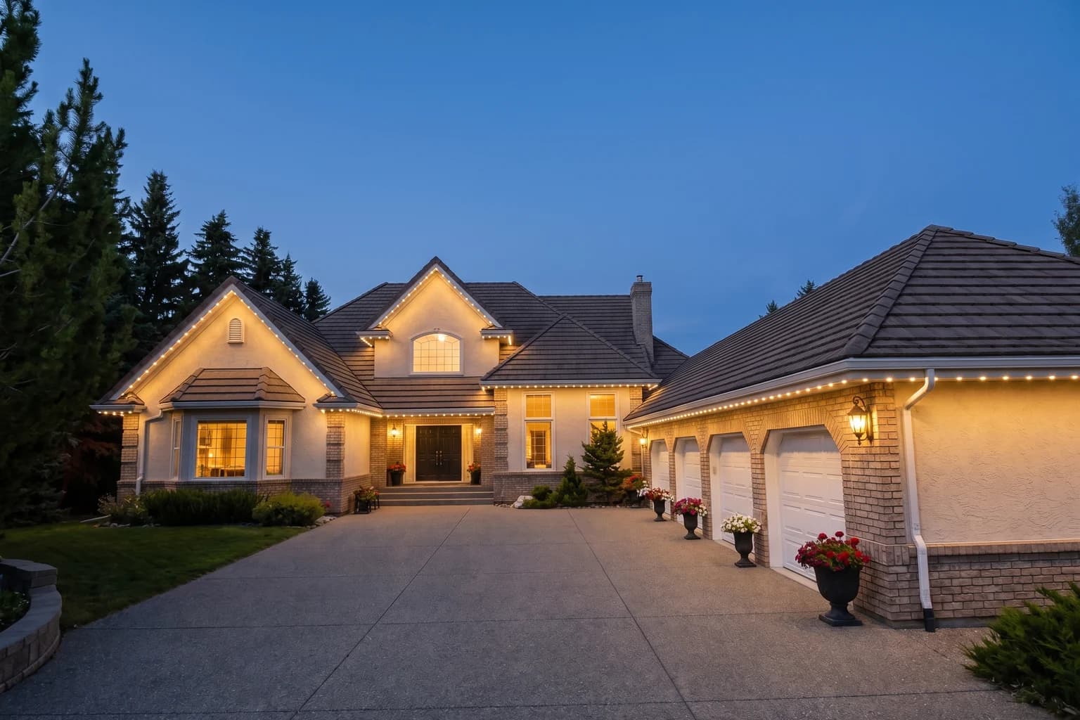 The same home at dusk with a warm white glow along every roofline and the garage wing